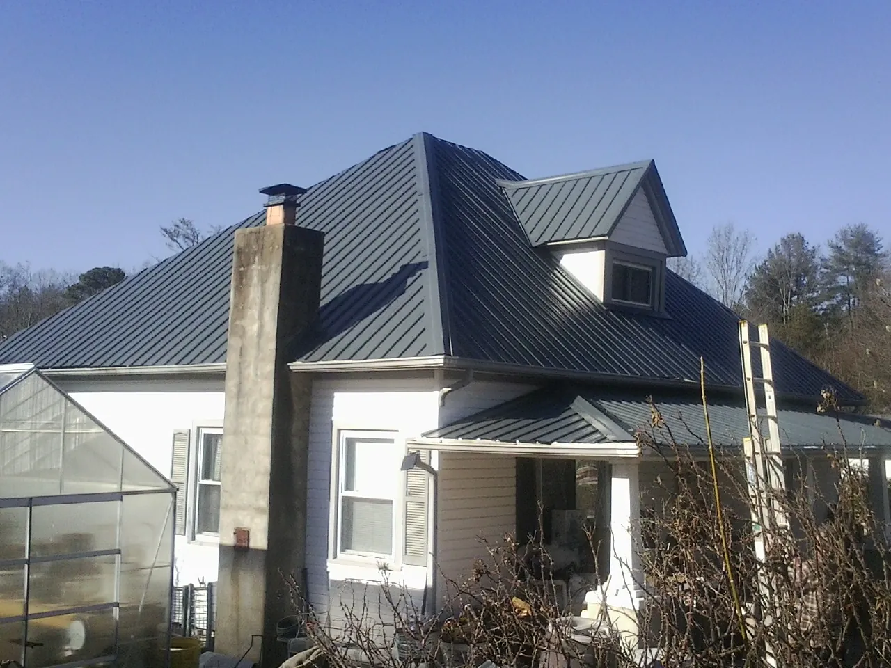Dark blue standing seam metal roof on a white farmhouse with dormer — Slate & Tile Roof Repair by Roofing Brothers in Heath Springs