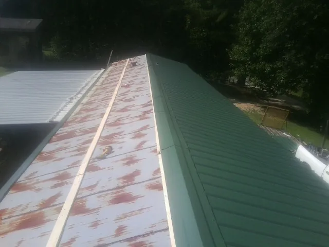 Old rusted panels beside newly installed green metal roofing — Wind Damage Roof Repair by Roofing Brothers in Heath Springs