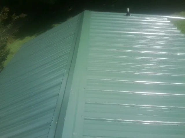 New green metal panels meeting at the ridge of a roof — Flat Roof Repair work by our crew in Heath Springs
