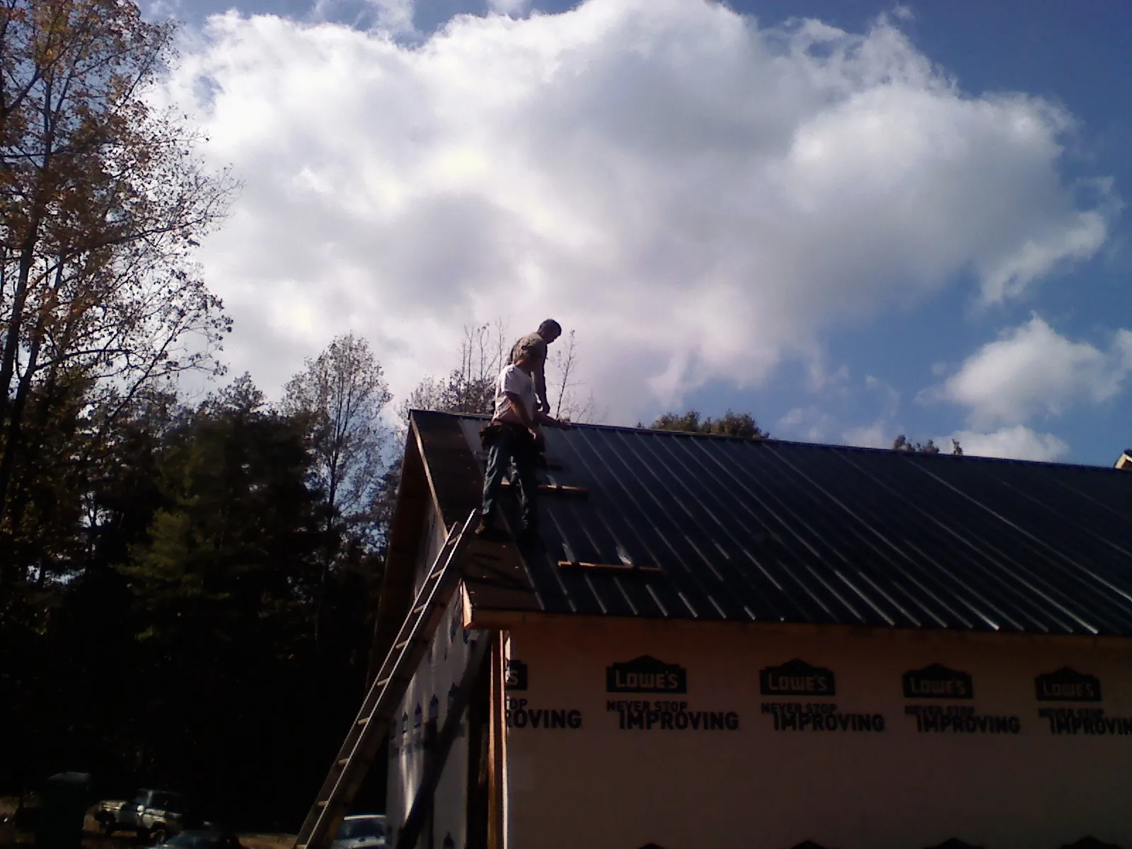 Roofer fastening dark metal panels high against a cloudy sky, from a Roof Inspection job in Heath Springs