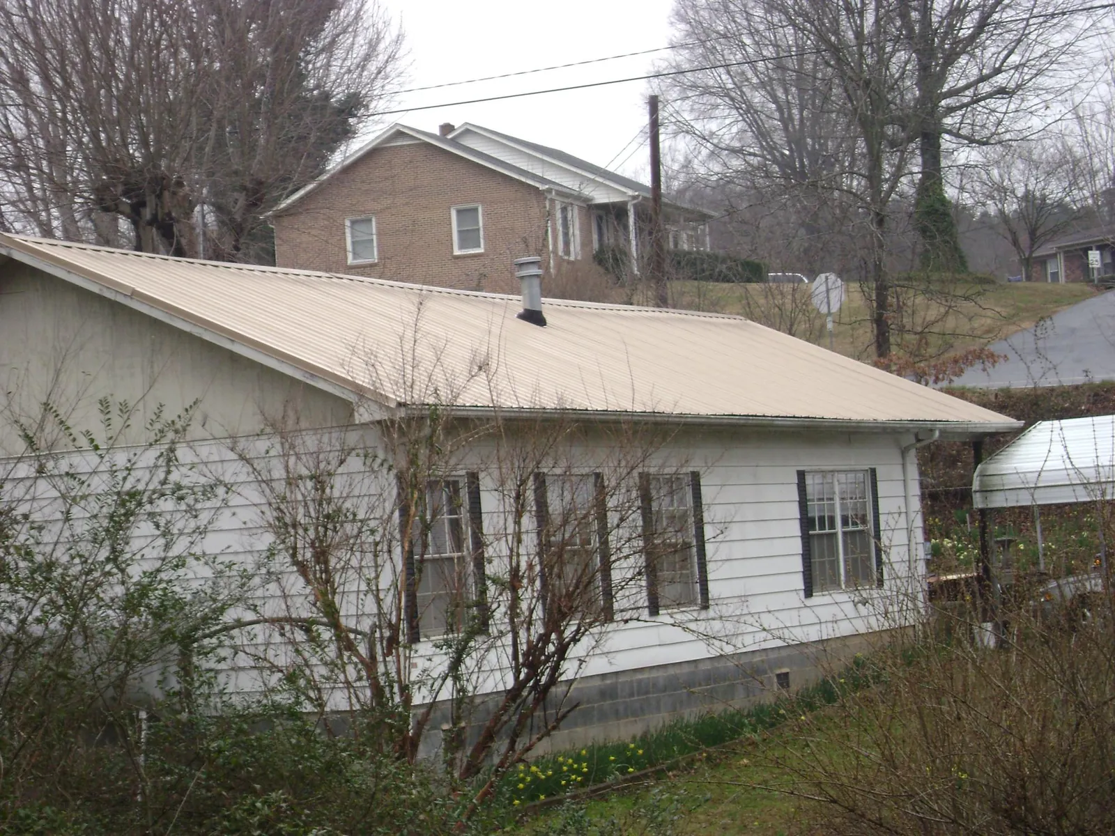 Tan metal roof on a white sided house set into a hillside — Commercial Roofing by Roofing Brothers in Heath Springs